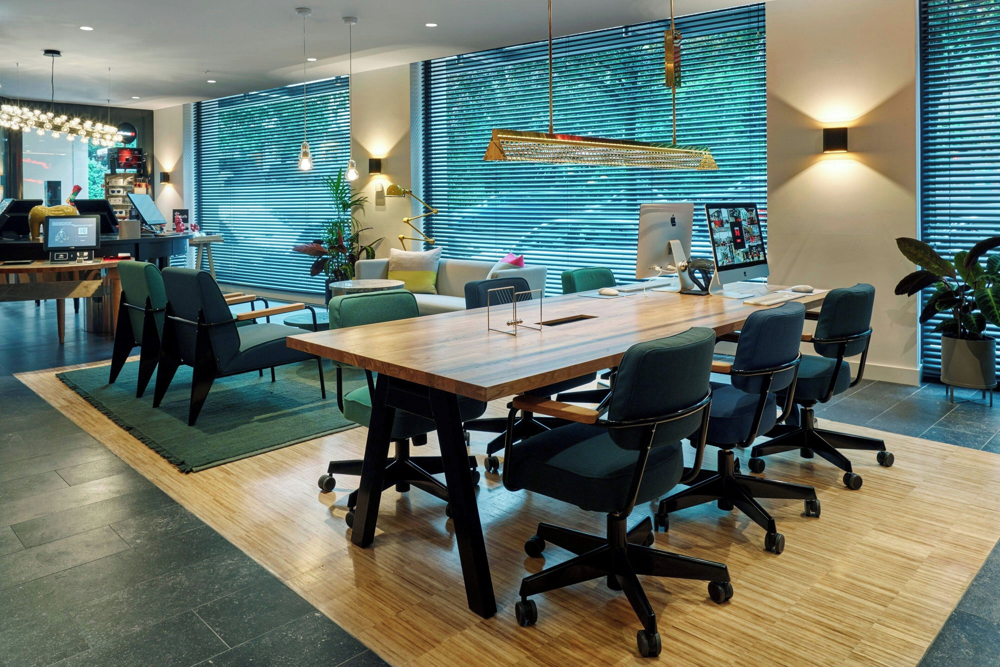 A modern office space with a long wooden table, black office chairs, and multiple computer monitors.