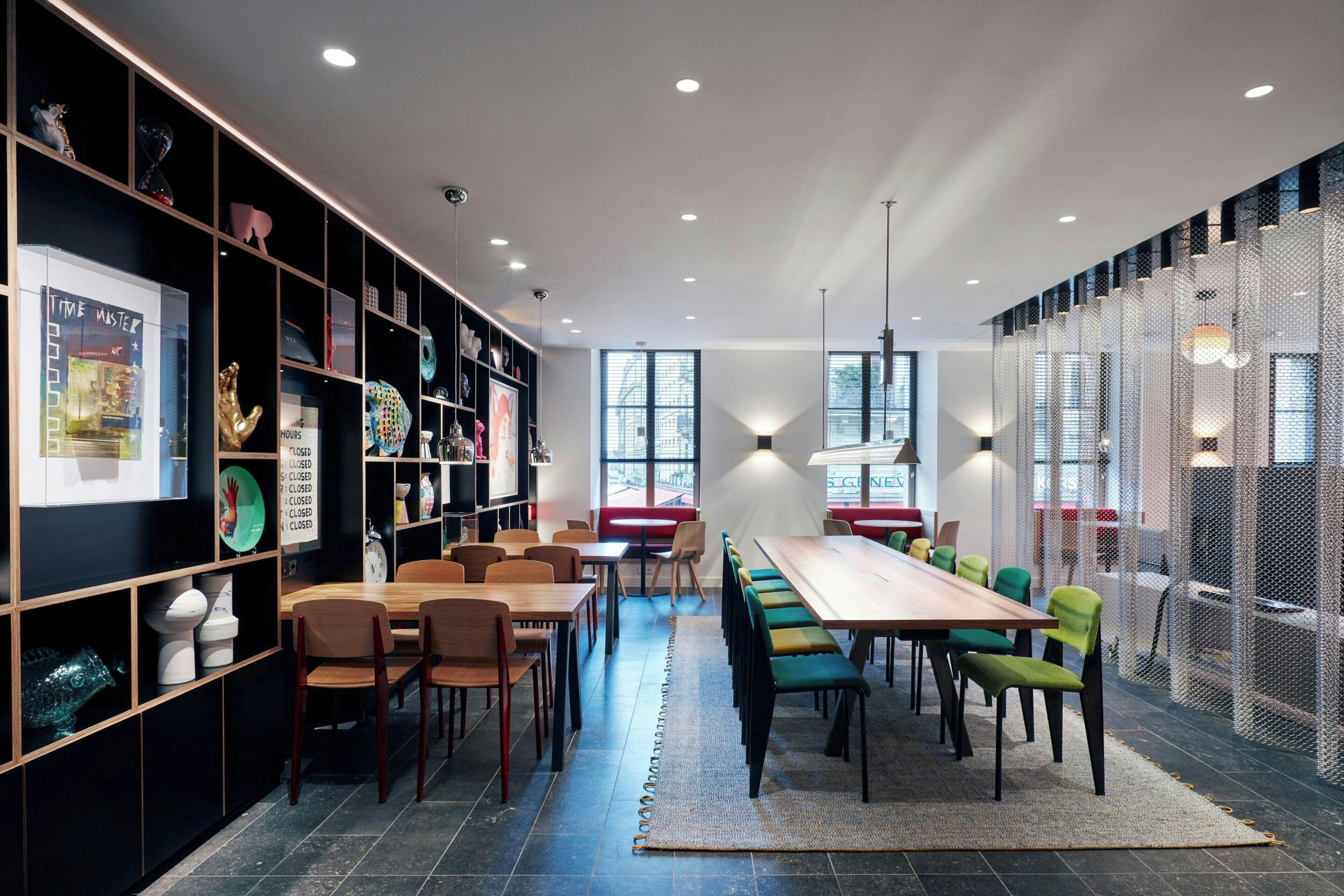 Un espace repas moderne avec une longue table en bois, plusieurs chaises et une bibliothèque contenant divers objets.