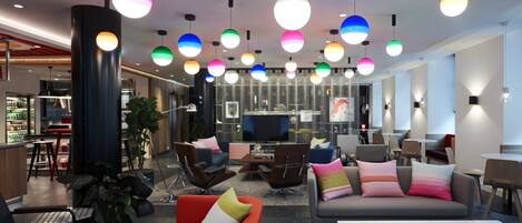 A modern lounge area with multiple seating options, a large flat-screen TV, and colorful pendant lighting.