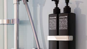 A shower with chrome fixtures and two black bottles labeled 'citizenAM' and 'citizenPM' on a wall.