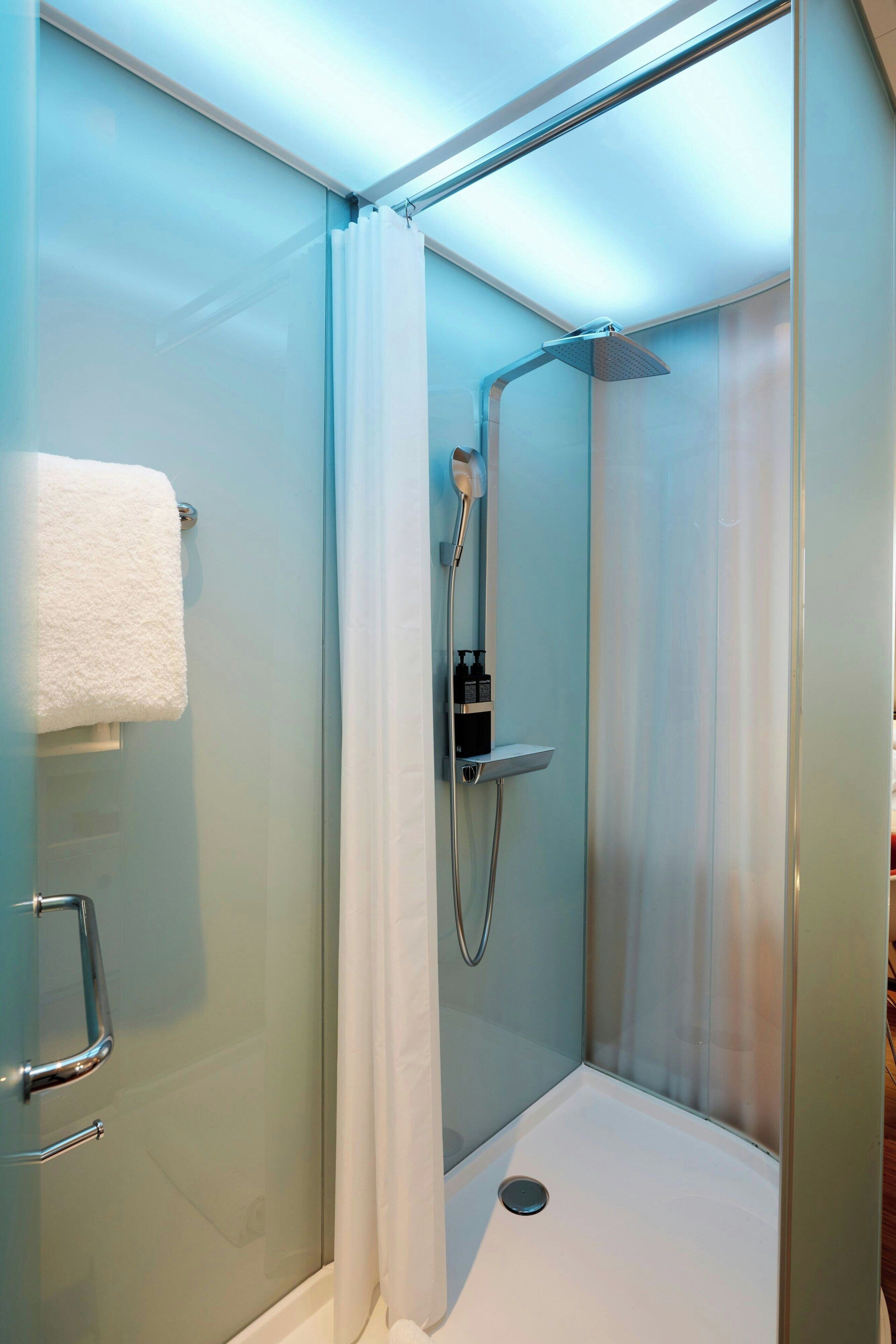 A glass-enclosed shower area with a handheld showerhead and a wall-mounted control panel.