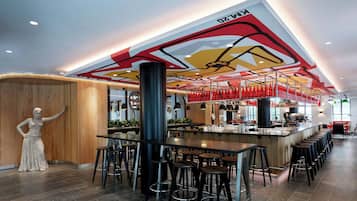 Zona de bar moderna con una barra larga y varios taburetes, un techo decorativo y una estatua de una mujer.