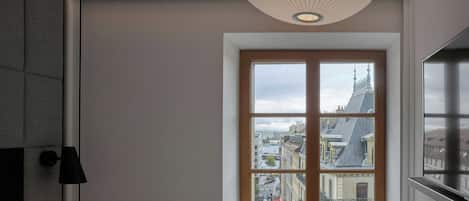 Ein Zimmer mit großem Fenster, einer modernen Pendelleuchte und Blick auf eine Stadtlandschaft.