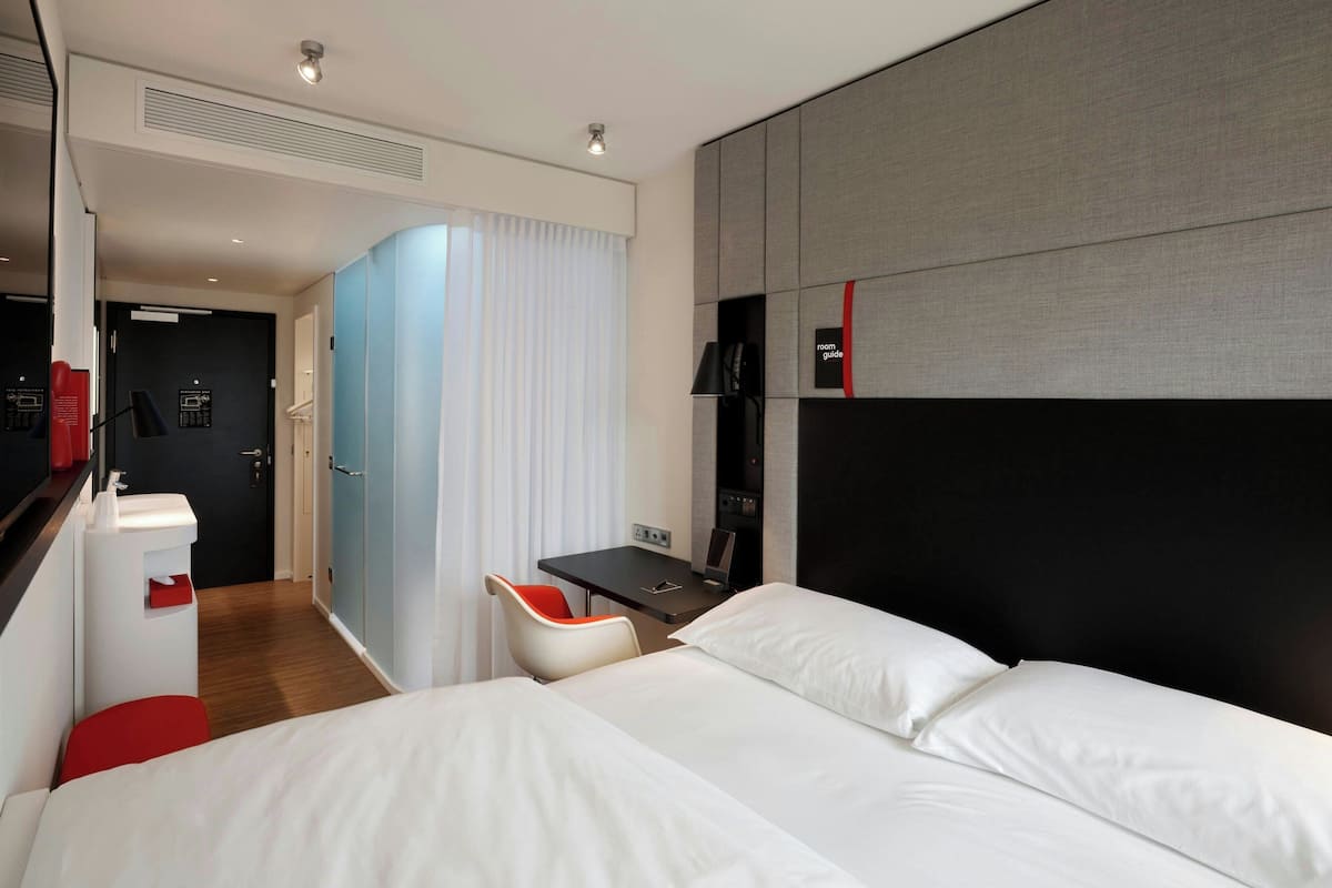 Una habitación de hotel moderna con una cama grande, un escritorio con una silla, una mesita pequeña y un armario.