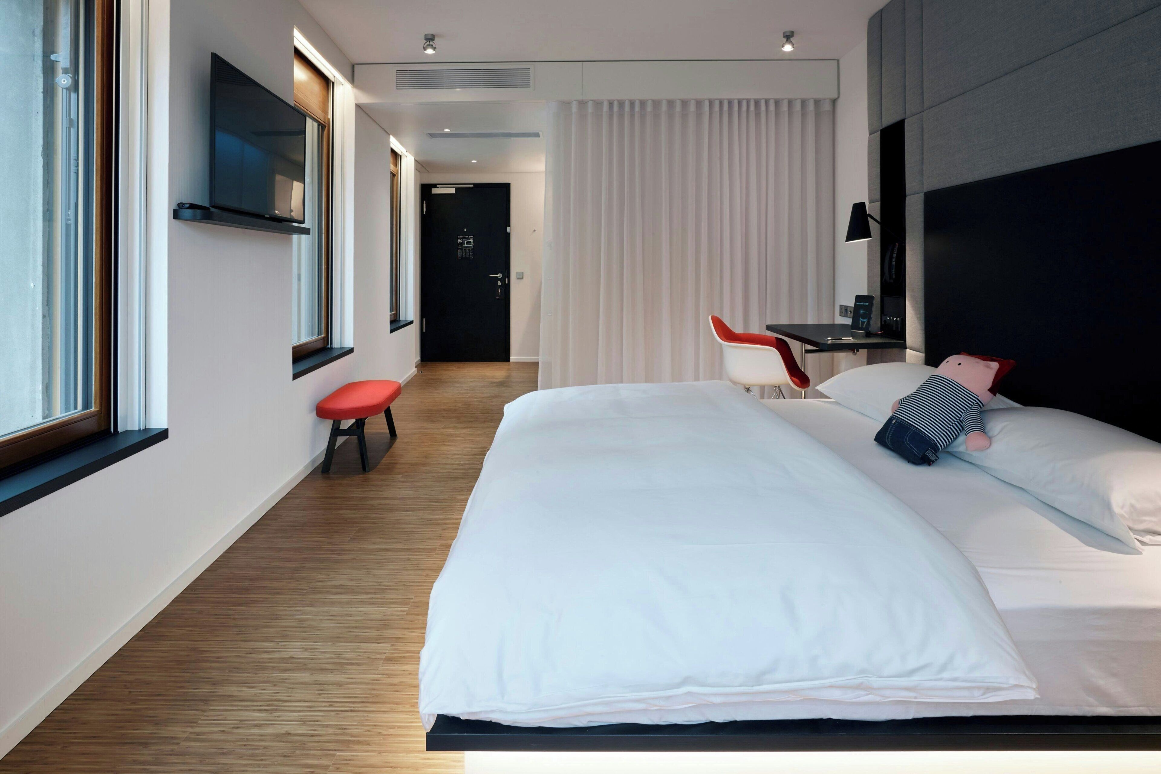 Una habitación de hotel moderna con una cama grande, un escritorio, una silla y un televisor montado en la pared.