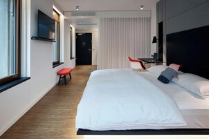 Una habitación de hotel moderna con una cama grande, un escritorio, una silla y un televisor montado en la pared.