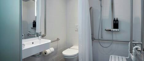 Un baño moderno con lavamanos, inodoro y zona de ducha blancos.