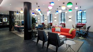 Un moderno vestíbulo de hotel con un sofá rojo, sillas negras y luces colgantes de colores.