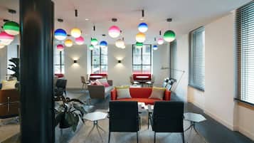 A modern living room with a sofa, chairs, and a coffee table. There are colorful pendant lights and a large black column.