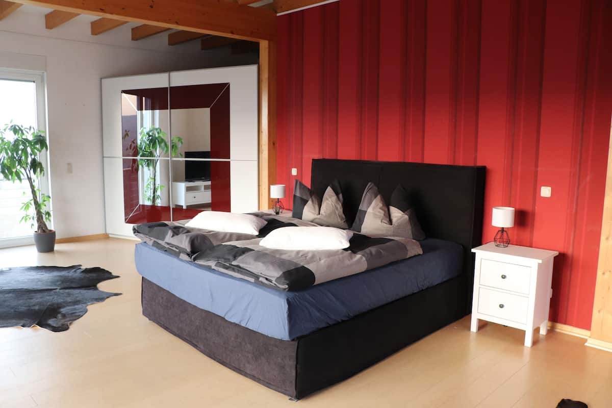 A modern bedroom with a large bed, a nightstand, a mirror, and a potted plant.