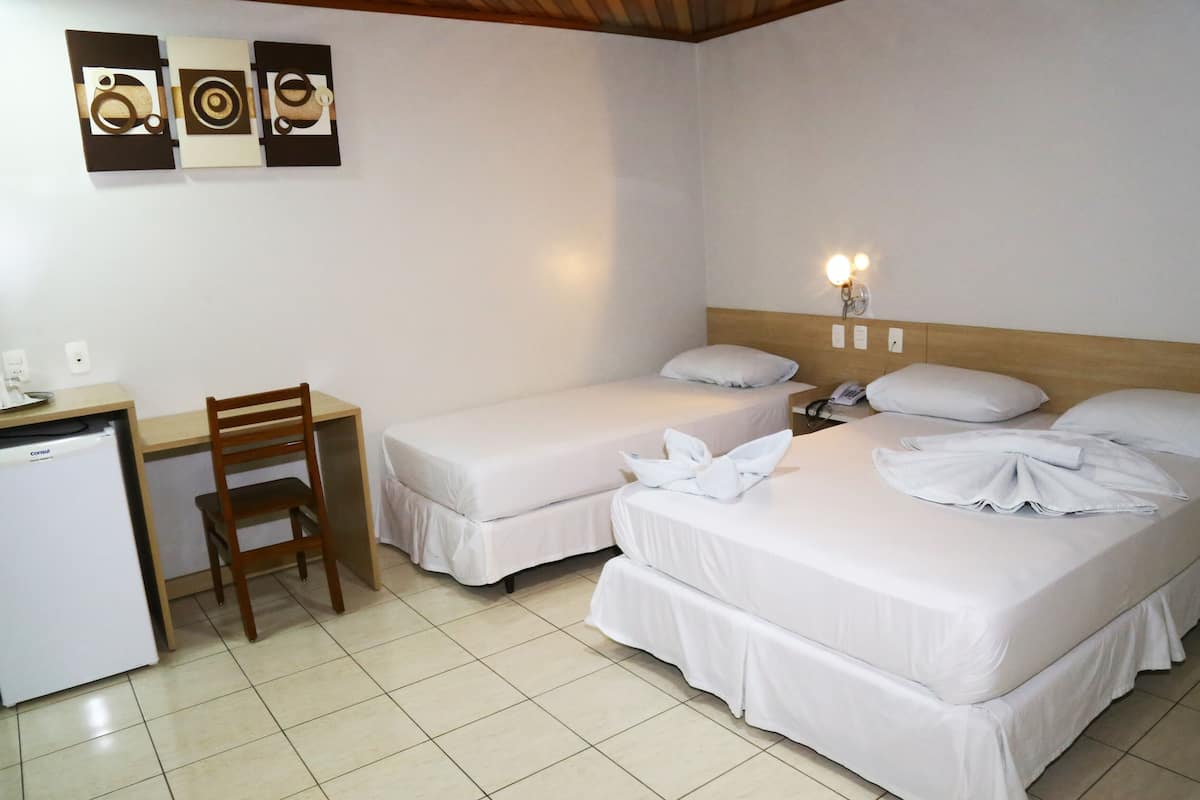 Une chambre d’hôtel avec deux lits, un bureau, une chaise, un réfrigérateur et des œuvres d’art murales.