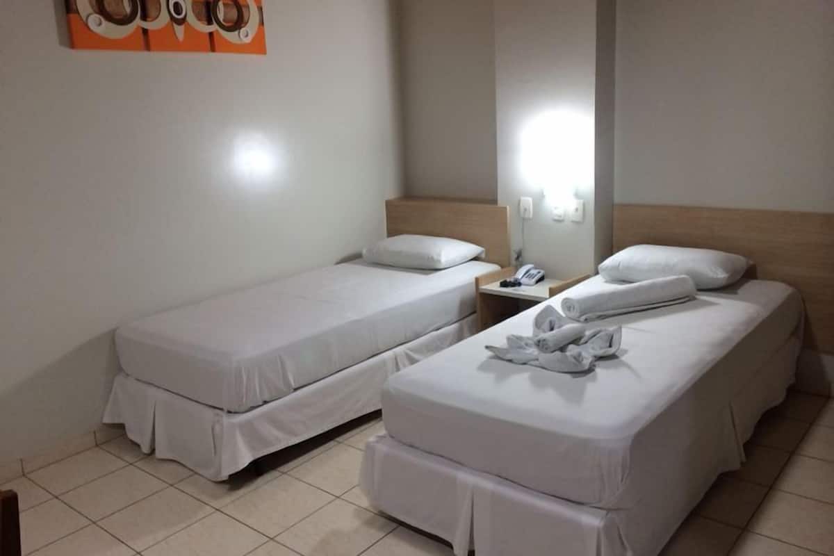 Une chambre d’hôtel avec deux lits simples, une table de chevet avec un téléphone et un miroir fixé au mur.