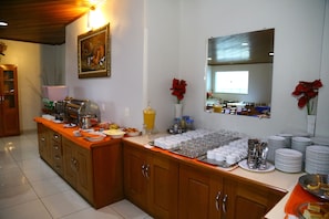 A buffet setup with a variety of food items and beverages, a wooden cabinet, and a painting on the wall.