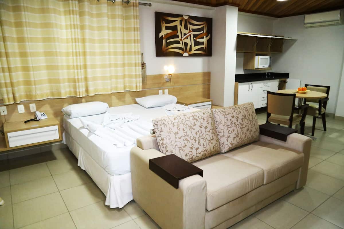 Une chambre d’hôtel comprenant un lit, un canapé, un bureau, une chaise, une petite table et un coin cuisine équipé d’un four à micro-ondes.