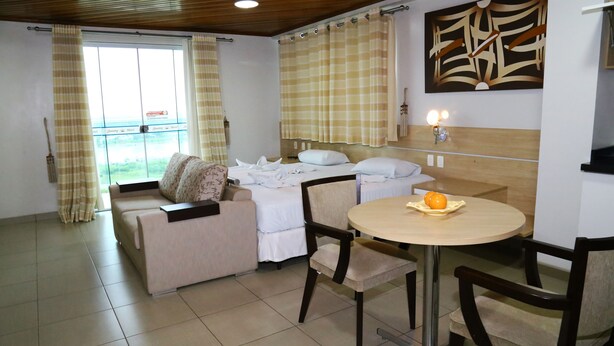 A hotel room with a bed, a sofa, a dining table with chairs, and a window with curtains. - Swamy Hotel (Cruzeiro do Sul)