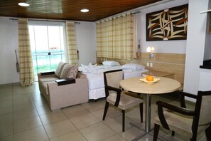 A hotel room with a bed, a sofa, a dining table with chairs, and a window with curtains. - Swamy Hotel (Cruzeiro do Sul)
