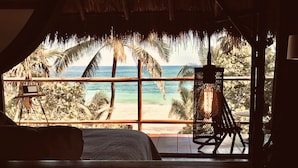 A room with a large window overlooking a beach, a bed, and a hanging chair. - Libelula Tulum Beachfront Hotel (Tulum)