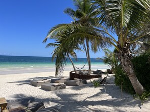 A beach with a hammock, lounge chairs, and a small table.