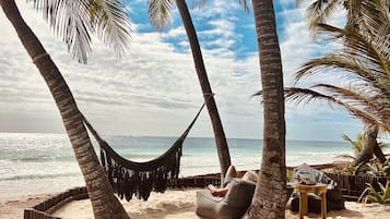 Escena de playa con una hamaca, una silla de descanso y una valla de madera.