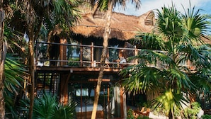 A two-story building with a thatched roof, surrounded by lush tropical vegetation. - Libelula Tulum Beachfront Hotel (Tulum)