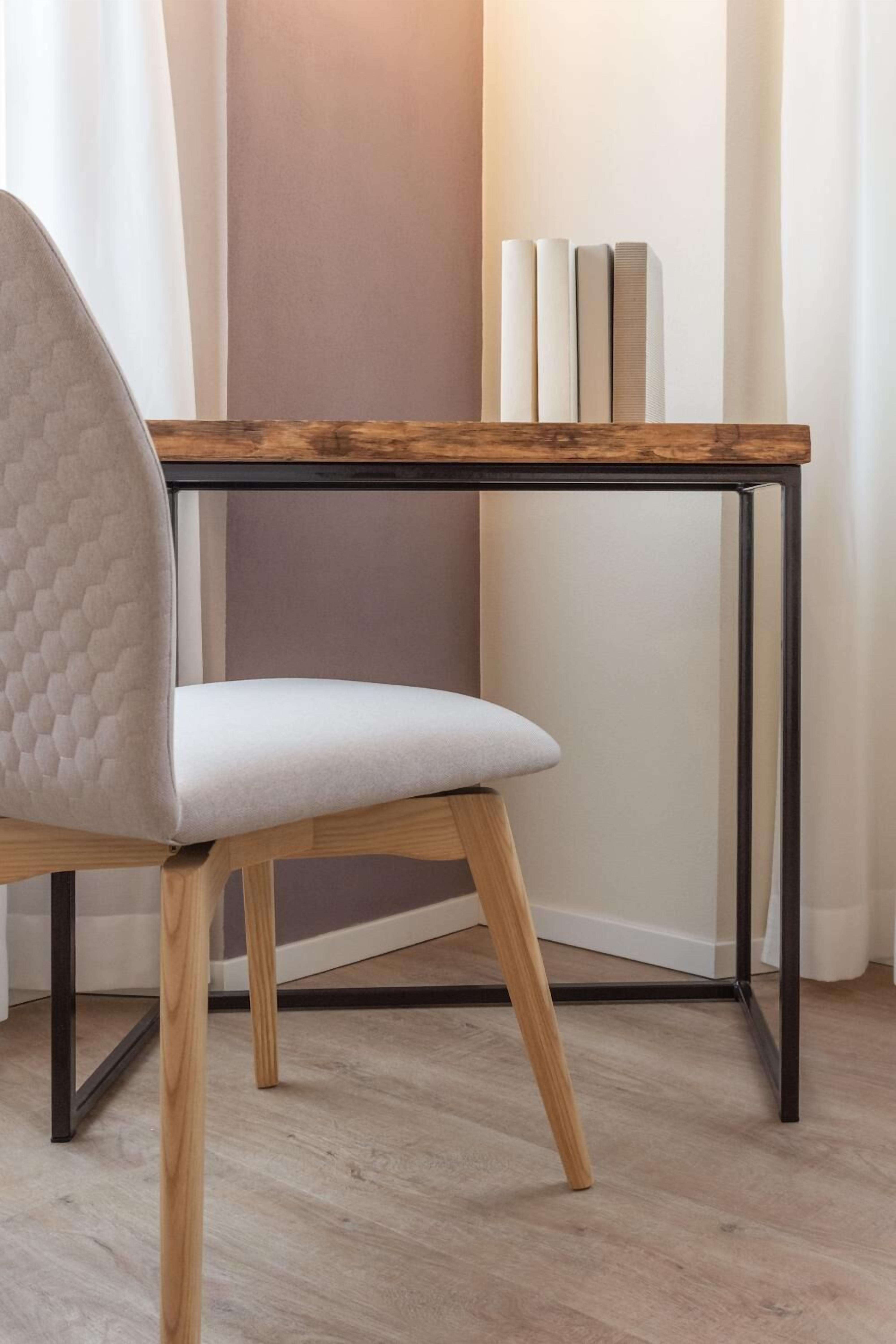 A modern chair with a quilted backrest and light-colored upholstery, positioned at a wooden table with a metal frame.
