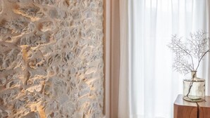 Ein Zimmer mit einer strukturierten Steinwand, einem Holzschrank und einem Fenster mit durchsichtigen Vorhängen.
