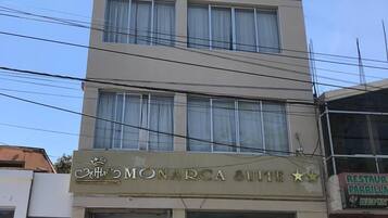 Un hotel llamado "Monarca Suite" con una fachada moderna, múltiples ventanas y una entrada visible con puerta de vidrio.