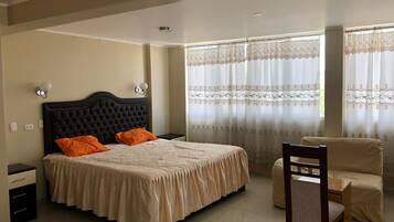 Un dormitorio con una cama grande, dos mesitas de noche, una silla y un ventanal con cortinas.