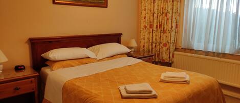 A hotel room with a bed, a nightstand, a lamp, a painting on the wall, and a window with curtains.