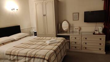 Une chambre d’hôtel comprenant un lit, un bureau avec un miroir, une commode avec des tiroirs, un téléviseur à écran plat et un luminaire fixé au mur.