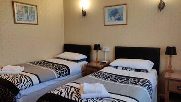 Ein Hotelzimmer mit zwei Betten, jeweils mit einer zebra-gemusterten Bettdecke, weißen Kissen und gefalteten Handtüchern. An den Wänden befinden sich Wandlampen und gerahmte Bilder.