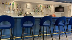 A bar area with a white tiled backsplash, multiple liquor bottles, and blue bar stools. - The Arundel Park Hotel (Arundel)