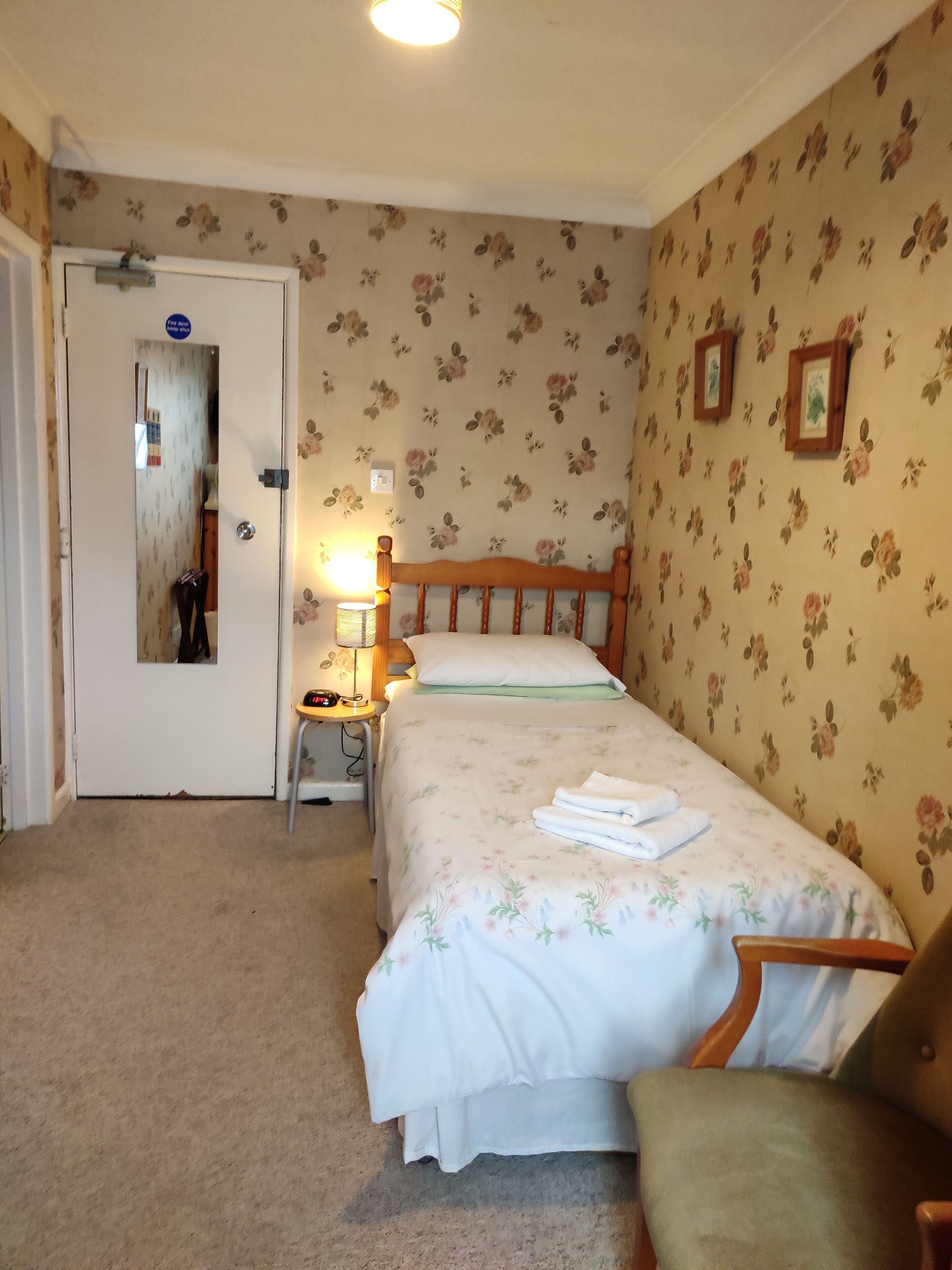 Ein Schlafzimmer mit Bett, Stuhl, Nachttisch, Lampe und einer Tür.