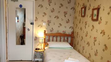 Ein Schlafzimmer mit Bett, Stuhl, Nachttisch, Lampe und einer Tür.