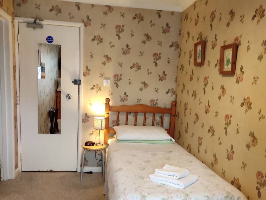 Ein Schlafzimmer mit Bett, Stuhl, Nachttisch, Lampe und einer Tür.