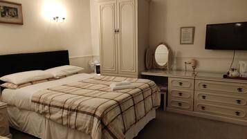 A bedroom with a bed, a dresser, a vanity with a mirror, and a television on the wall.