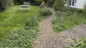 A garden with a paved pathway, a picnic table, and a white building with windows. - The Arundel Park Hotel (Arundel)