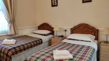 A hotel room with two beds, each with a plaid bedspread and white pillows, a nightstand with a lamp, and a framed picture on the wall.