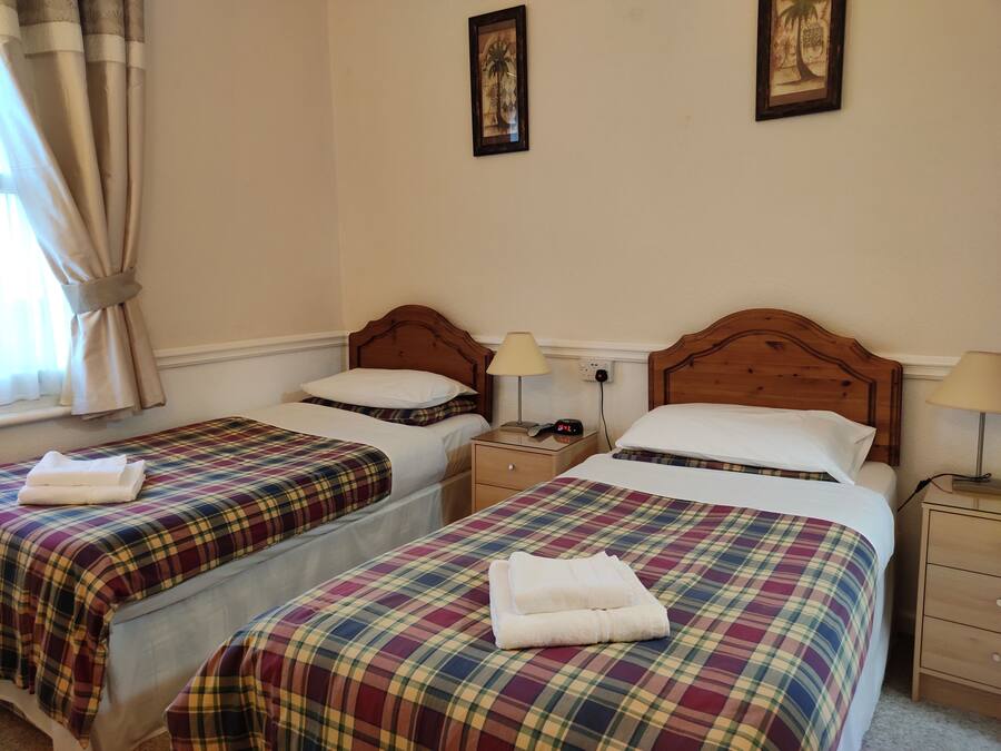 A hotel room with two beds, each with a plaid bedspread and white pillows, a nightstand with a lamp, and a framed picture on the wall.