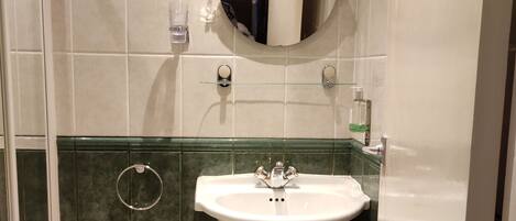 Un baño con lavamanos pedestal, espejo, toallero y cesto de basura.