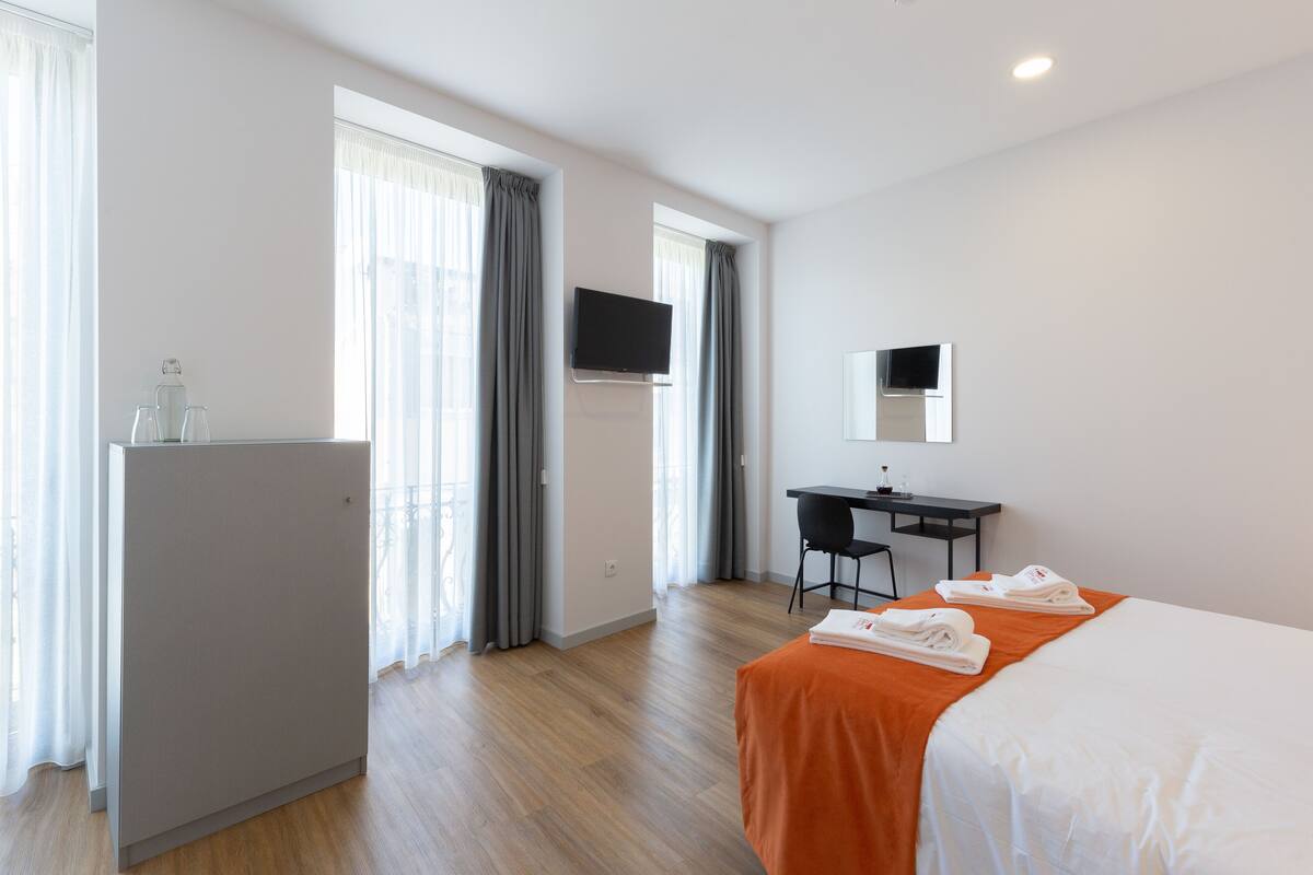 A hotel room with a bed, a desk, a TV, and a minibar.