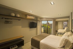 A modern hotel room with a bed, a TV, a balcony, and a view of the city.
