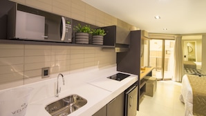 A modern kitchen with a microwave, sink, and countertop. There is a small dining area with a table and chairs. The room has a sliding glass door leading to a balcony. - Infinity at the Sea by Welkom (João Pessoa)