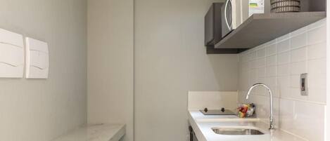 A modern kitchen with a white countertop, stainless steel sink, and a microwave on a shelf.