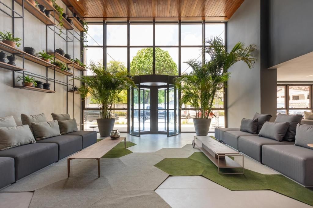 Un interior moderno con una puerta giratoria central, sofás grises, una mesa de centro y plantas en macetas.