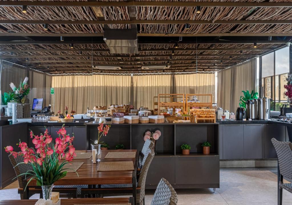 A modern restaurant with a wooden ceiling, a counter with various food items, and a dining area with tables and chairs.