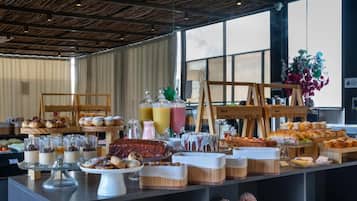 Un bufé con diversos alimentos y postres, una estructura de madera y un gran ventanal al fondo.