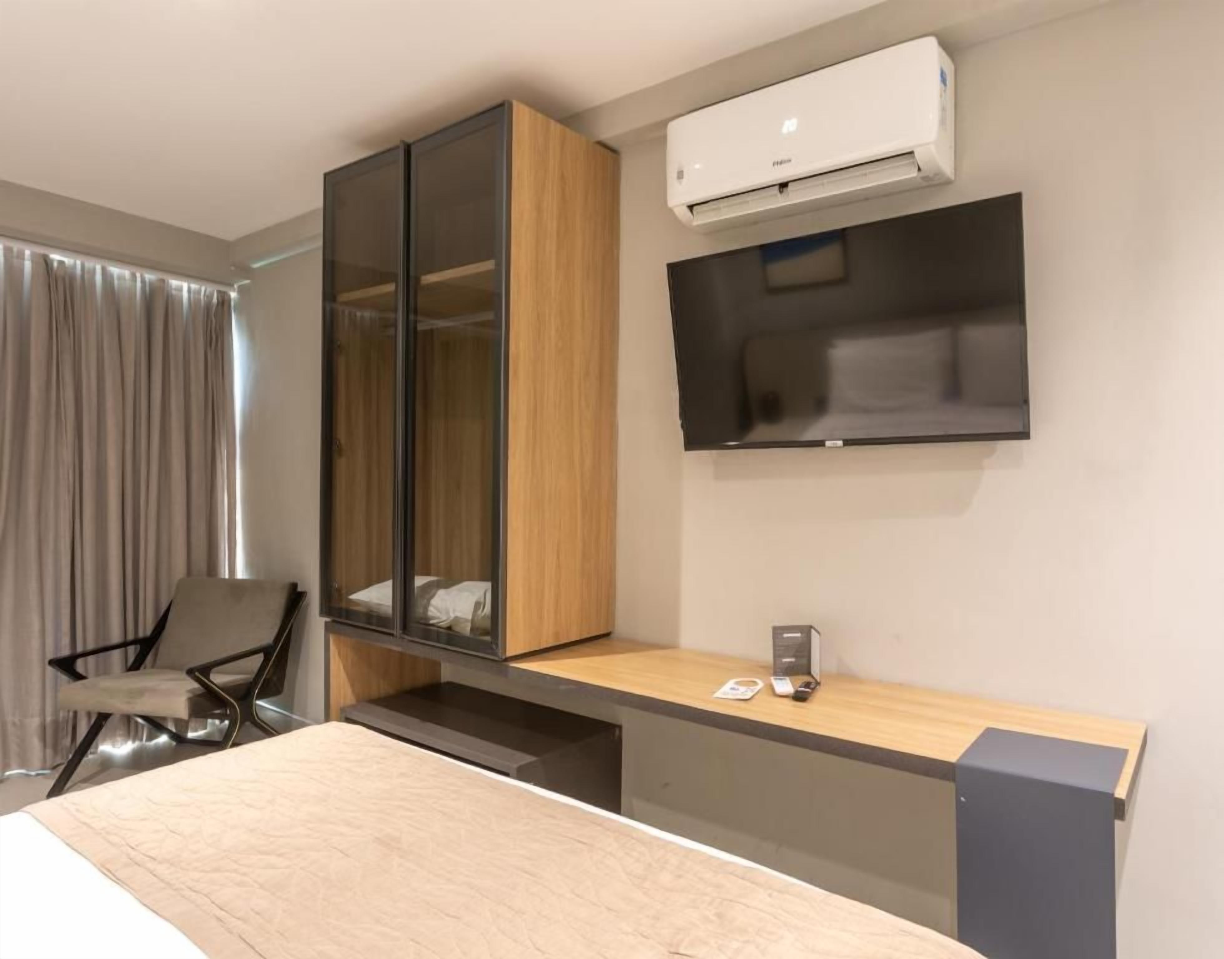 Une chambre d’hôtel moderne équipée d’un lit, d’un bureau, d’une chaise, d’une armoire, d’un téléviseur à écran plat et d’un système de climatisation.
