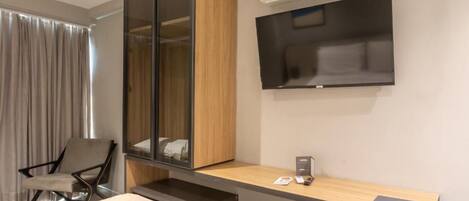 Habitación de hotel moderna con cama, escritorio, silla, armario, televisor de pantalla plana y aire acondicionado.