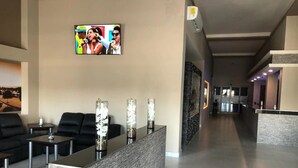 A modern lobby with a reception desk, black leather seating, and a television screen displaying a performer. - Hotel Plaza Arteaga (Monterrey)